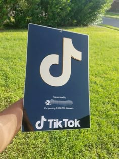 someone holding up a sign that says tiktok in front of some trees and grass