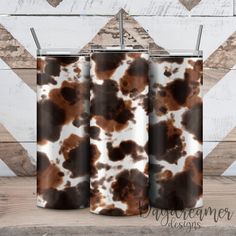 two brown and white cow print tumblers sitting next to each other on a wooden table