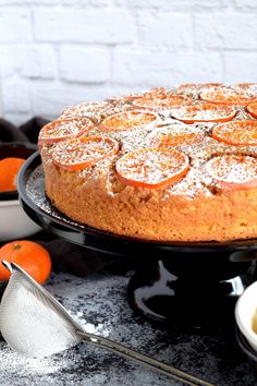 an orange cake with powdered sugar on top is sitting on a black platter