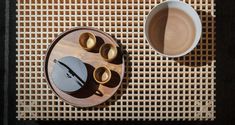 an overhead view of a wooden tray with cups and spoons next to it on a woven mat