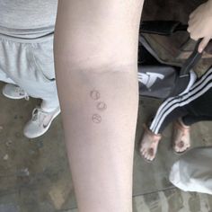 two people standing next to each other with tattoos on their arms and legs, one has a small circle tattoo on it's left arm