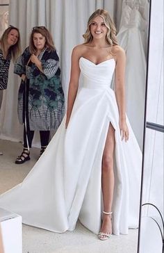 a woman standing in front of a mirror wearing a white dress with high slits