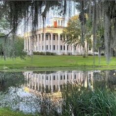 a large white house sitting on top of a lush green field next to a lake