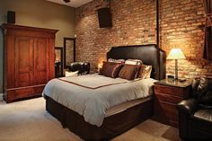 a bedroom with a bed, chair and brick wall