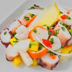 a white plate topped with shrimp and veggies next to a lemon wedge on top of a table