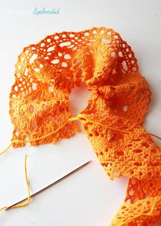 an orange crochet scarf is laying on a white surface next to a pair of scissors