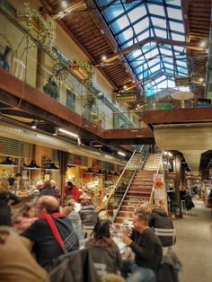 people are sitting at tables and eating in a large room with high ceilings that have glass windows on the ceiling