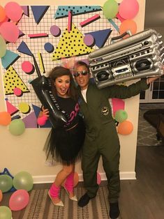 a man and woman posing for a photo in front of a party backdrop with balloons