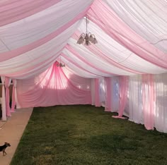 a pink and white tent set up for a wedding with a dog running in the grass