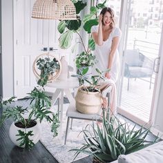 a woman standing next to a plant in a living room with lots of greenery