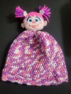 a crocheted doll with pink hair is laying on a black surface