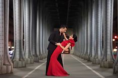 a man and woman dressed in red posing for a photo under a bridge at night