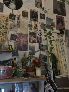 a wall covered with pictures and plants in front of a camera on a table next to a window