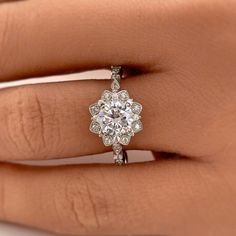 a woman's hand holding an engagement ring with a flower design on the side