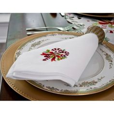 a place setting with white napkins and gold rimmed plates, decorated with christmas decorations