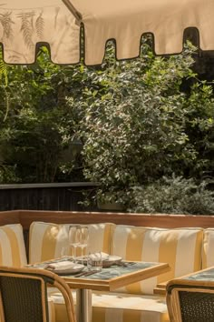 an outdoor seating area with tables, chairs and umbrellas over the table in front of trees