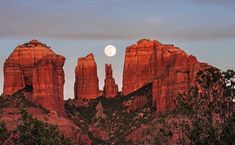 the full moon is setting over red rock formations