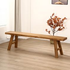 a wooden bench sitting on top of a hard wood floor next to a vase filled with flowers