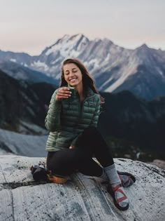 a woman sitting on top of a rock with mountains in the background