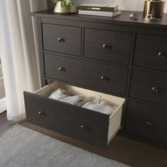 a dresser with two drawers and a vase on the top shelf, next to a window