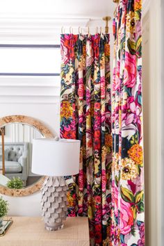 the curtains in this room are brightly colored and have colorful flowers on them, as well as a round mirror