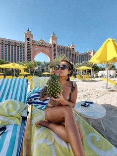 a woman is sitting on the beach with a pineapple in her hand and wearing sunglasses