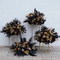 three gold and black wedding bouquets on display in front of a white wall with wood flooring