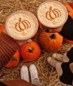 two people are holding cups with pumpkins on them in the hay next to their feet