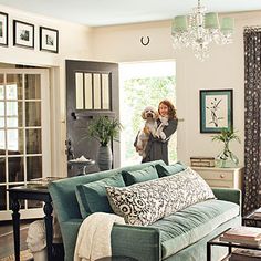 a woman is holding a dog in her arms while standing next to a couch and coffee table