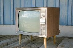 an old tv sitting on top of wooden legs in front of a blue painted wall