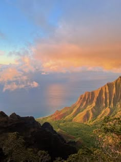 the mountains are covered in green vegetation and clouds as the sun sets over the ocean