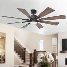 a ceiling fan with five wooden blades in a living room next to stairs and a fireplace