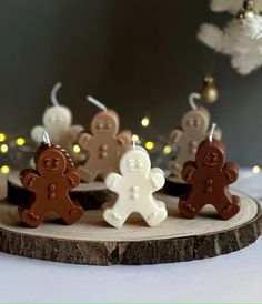 four small gingerbread men are on a wood slice with christmas lights in the background