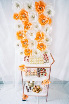 an orange and white flower arrangement is displayed on a stand with sweets in front of it