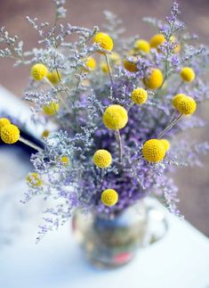 a vase filled with lots of yellow flowers on top of a table next to a window