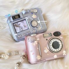 two cameras sitting next to each other on top of a white fur covered floor with beads