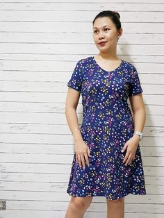 a woman standing in front of a white wall wearing a blue dress with flowers on it