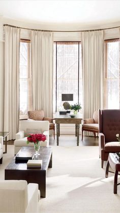 a living room with couches, chairs and tables in front of two large windows