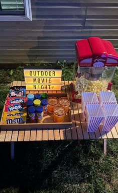 an outdoor movie party with popcorn, drinks and snacks on a picnic table in the grass