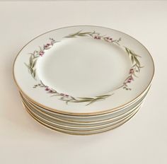 a stack of white and gold plates with purple flowers on the rim, all stacked up