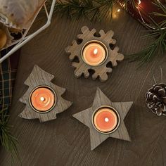 three wooden snowflakes with candles in them on a table next to pine cones