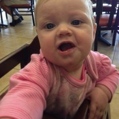 a baby sitting in a high chair with its mouth open and looking at the camera