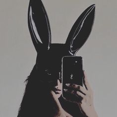 a person holding up a cell phone in front of a rabbit's head with ears