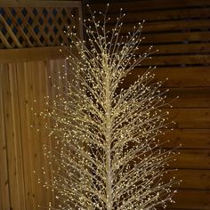 a white christmas tree with lights on it in front of a wooden wall and fence