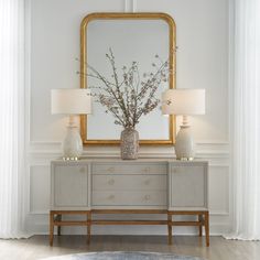 a vase with flowers sitting on top of a dresser next to two lamps and a mirror