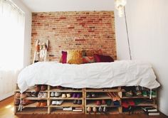 a bed with lots of shoes on it in a room next to a brick wall