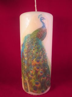 a lit candle with a painting of a peacock on it's front and side