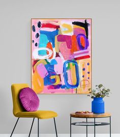 an abstract painting hangs on the wall next to two chairs and a table with a potted plant