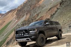 a gray ram truck parked on top of a dirt road in front of a mountain