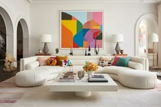 a living room filled with white furniture and lots of paintings on the wall above it